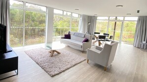 A spacious living room with a large window, a sofa, a coffee table, and a TV. - The Peninsula Grande (Karikari Peninsula)