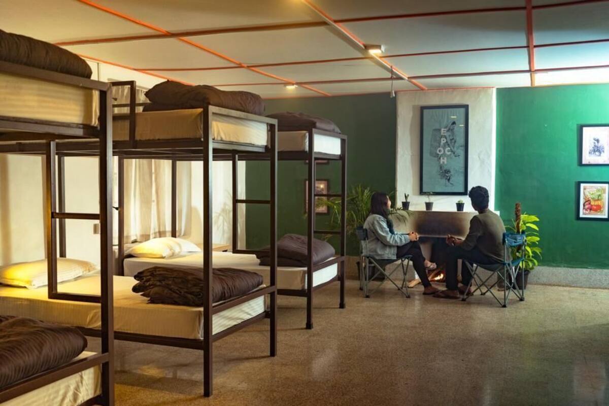 Quarto estilo dormitório com beliches, escrivaninha, cadeiras e parede verde com obras de arte.