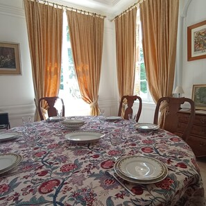 A dining room with a floral tablecloth, wooden chairs, and a chandelier. - Château de Heuqueville, 7-person gîte, Normandy between Giverny and Rouen (Heuqueville)