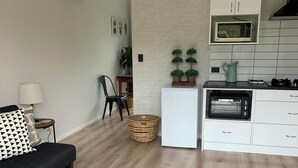 A modern living room with a sofa, a patterned rug, and a kitchen area with a microwave, oven, and cabinets. - Springcreek studio apartment  (Rapaura)