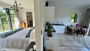A modern bedroom with a large bed, a small table with a candle, and a view of the kitchen area. - Springcreek studio apartment  (Rapaura)