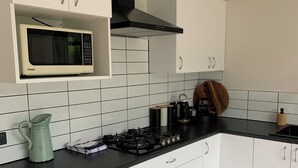 A modern kitchen with white cabinets, a black countertop, a microwave, a stove, and a coffee maker. - Springcreek studio apartment  (Rapaura)