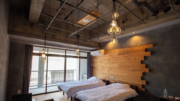 Un dormitorio moderno con dos camas, cabecero de madera, ventanas amplias y lámparas colgantes.
