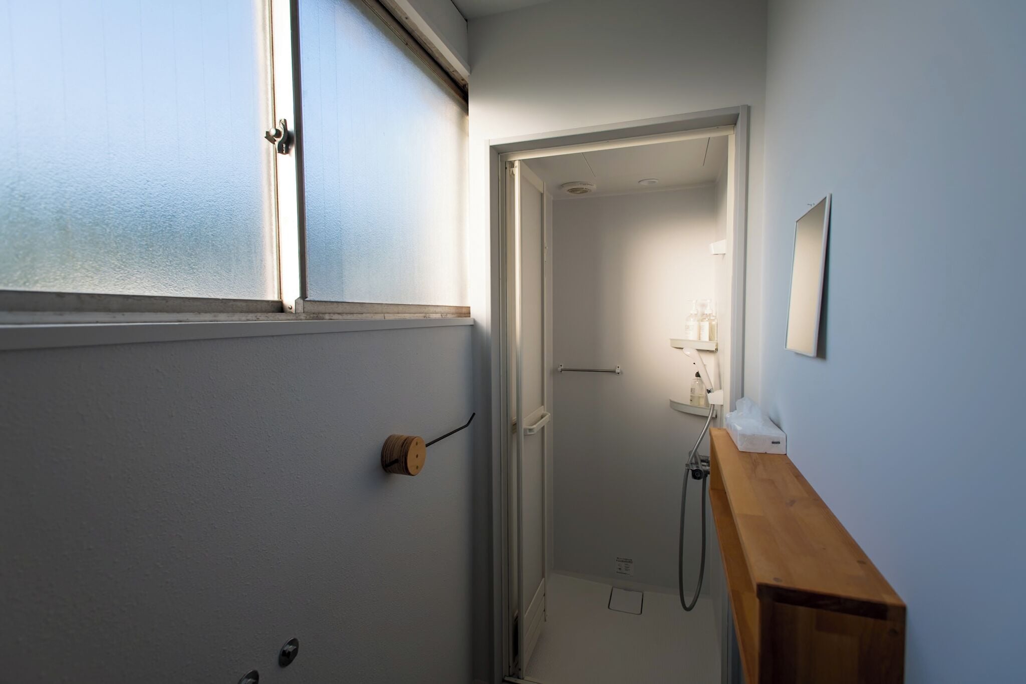 A narrow hallway with a wooden bench, a door leading to a bathroom, and a mirror on the wall.