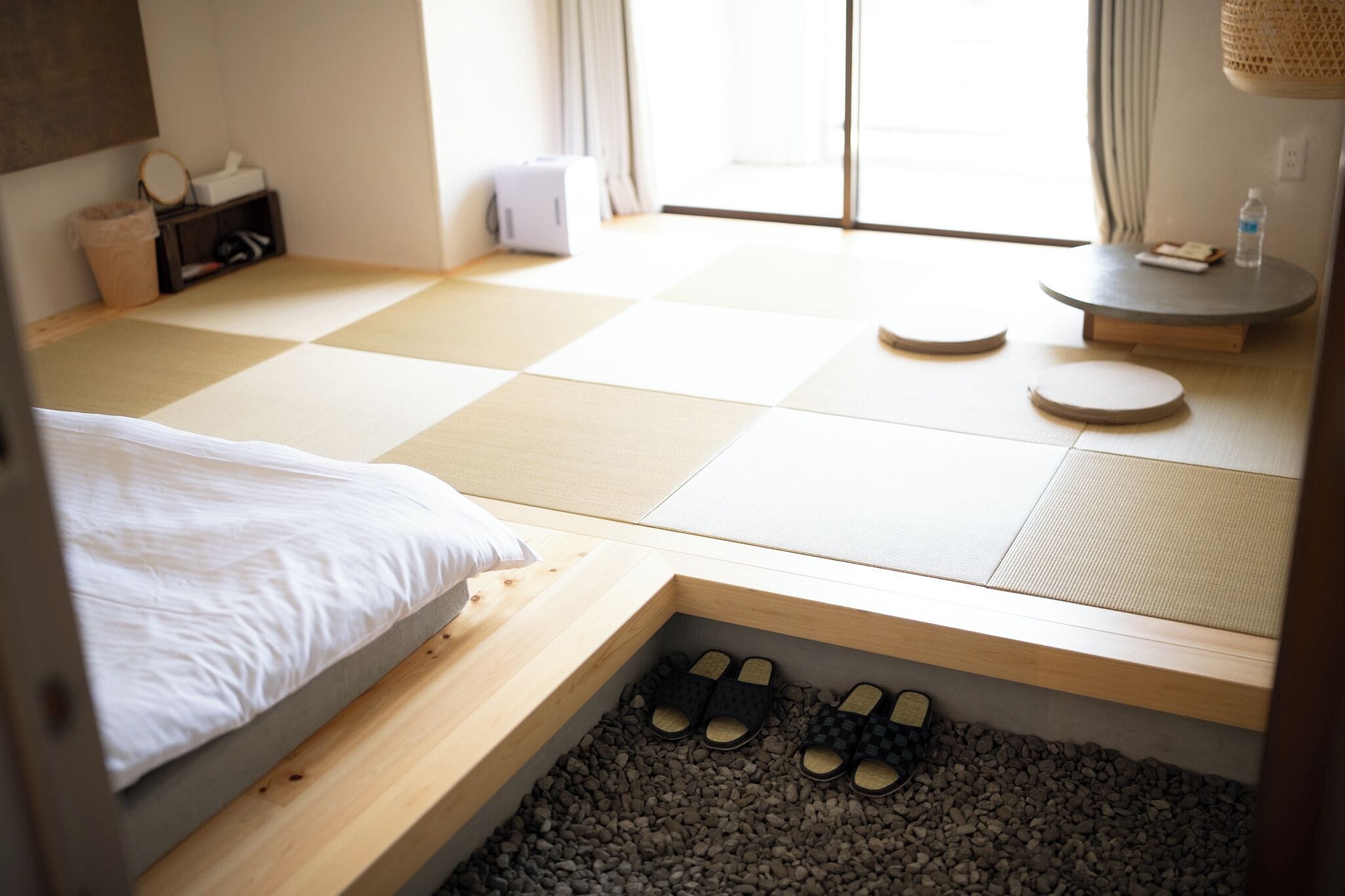 Habitación con estera de tatami, cama, zapatillas y una mesa pequeña con una botella.