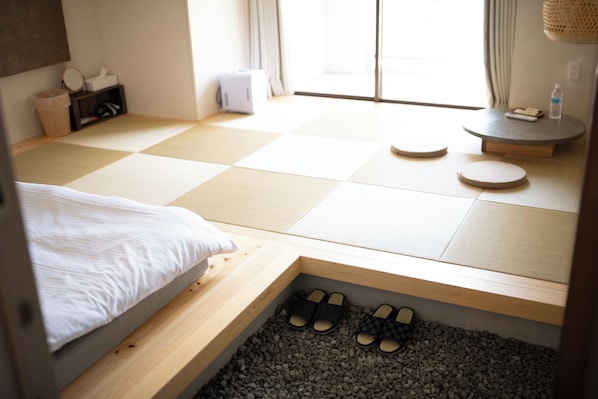 Habitación con estera de tatami, cama, zapatillas y una mesa pequeña con una botella.