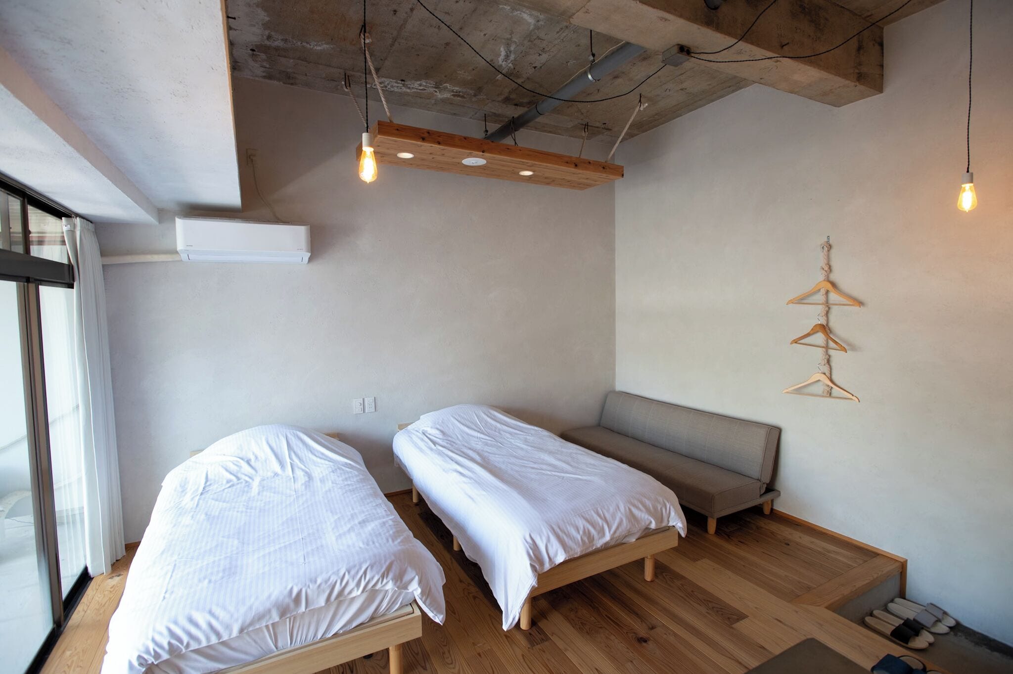 A minimalist bedroom with two single beds, a bench, and a wooden floor.