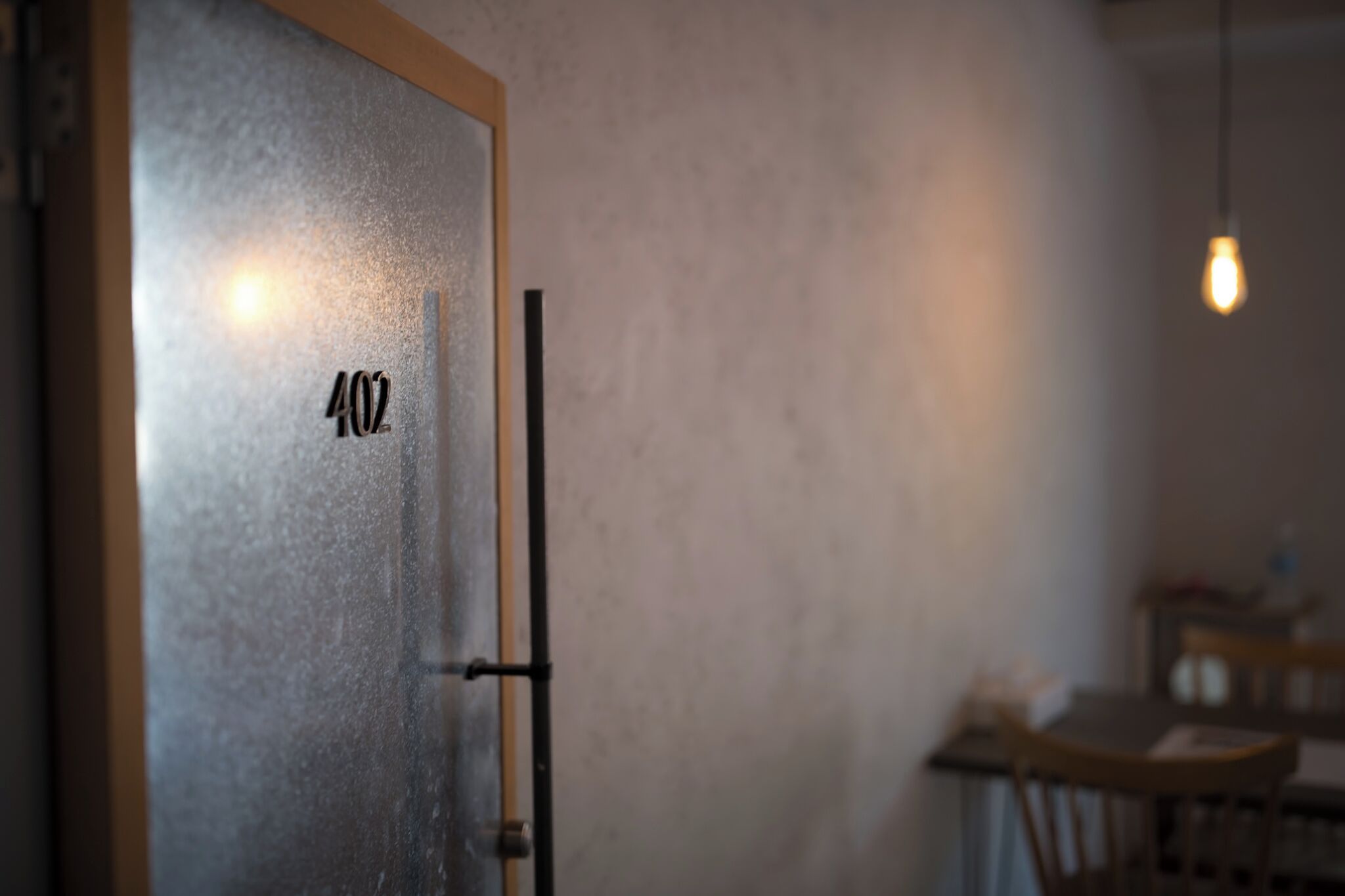 Une porte portant le numéro 402, un cadre de porte en bois et un luminaire visible à l’arrière-plan.