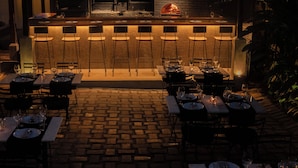 An outdoor dining area with a brick floor, bar with stools, and tables set for dining. - Havelock Place Bungalow (Colombo)