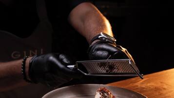 A person wearing black gloves holding a grater over a plate with food.