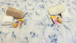 Un letto con copriletto a motivi floreali, due asciugamani arrotolati, una bottiglia di lozione, una saponetta e una piccola bottiglia di shampoo.