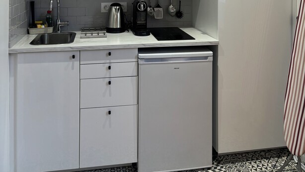 Una cucina compatta con mobili bianchi, un forno a microonde integrato, un lavello, una macchina da caffè e un’lavastoviglie.