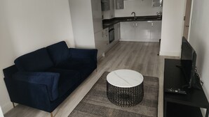 A modern living room with a dark blue sofa, a round coffee table, and a patterned rug. A TV is on a stand to the right. - Modern & Cozy 1bed Apartment Close to City Centre (Coventry)