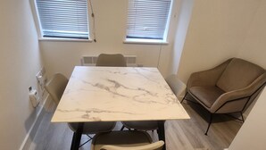 A room with a marble table, four chairs, a brown armchair, and two windows with blinds. - Modern & Cozy 1bed Apartment Close to City Centre (Coventry)