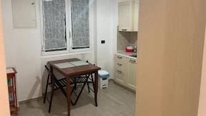 A small kitchen with a window, a table, and a trash bin.