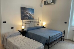 A bedroom with two beds, a nightstand with a lamp, a wall-mounted light fixture, and a painting of a celestial scene. - Casa Del Lupo, Vacation & Relax (Genova)
