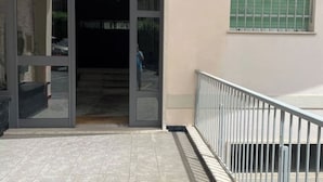 A building entrance with a glass door, a metal railing, and a window with a green shutter.