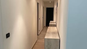 A narrow, well-lit hallway with a wooden floor and a light-colored bench at the end.