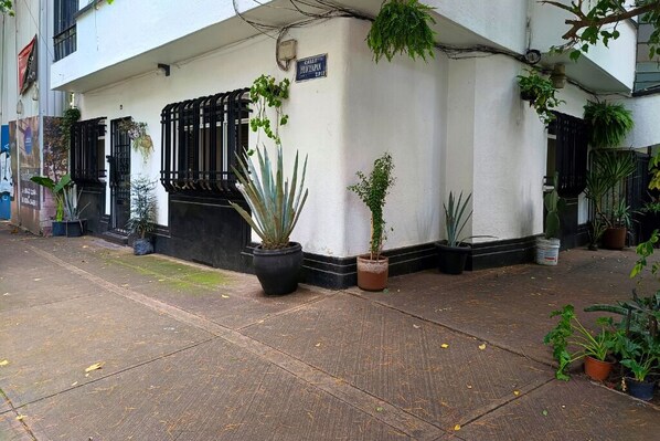 A building with a white facade, black window frames, and a sign reading "CAFE & RESTAURANT." There are potted plants on the sidewalk and a few on the building's exterior.