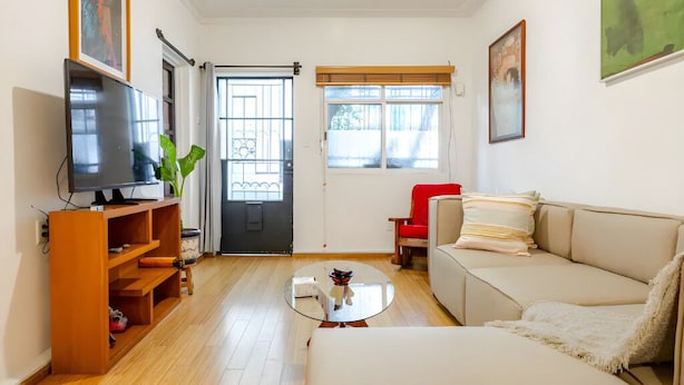 A living room with a sofa, a coffee table, a TV on a wooden stand, and a door with a window. - Ave Ámsterdam at Parque México (Mexico City)