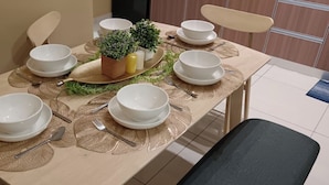 A dining table set with white bowls, plates, and cutlery, accompanied by a small potted plant and decorative placemats. - The Horizon Ipoh Dual L13A by Grab A Stay (Ipoh)
