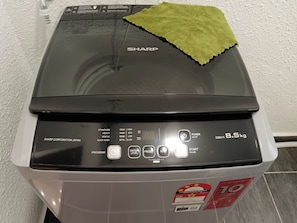 Vista frontal de una lavadora Sharp con un paño verde encima, mostrando diversas opciones de configuración e un indicador de peso de 8,5 kg.