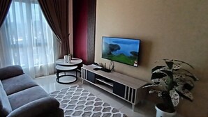 A living room with a sofa, a small round table, a TV on a stand, a potted plant, and a window with curtains. - The Horizon Ipoh Dual L13A by Grab A Stay (Ipoh)