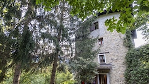 Ein Steinhaus mit Holztür und -fenstern, umgeben von Bäumen und einem Garten.
