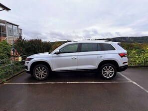 A white SUV parked in a parking lot with a building and trees in the background. - ReMo I Aare view I Business - Family - Terrace (Brugg)