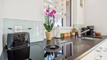 A modern kitchen with a black induction cooktop, a built-in oven, a window with blinds, and a potted orchid plant.