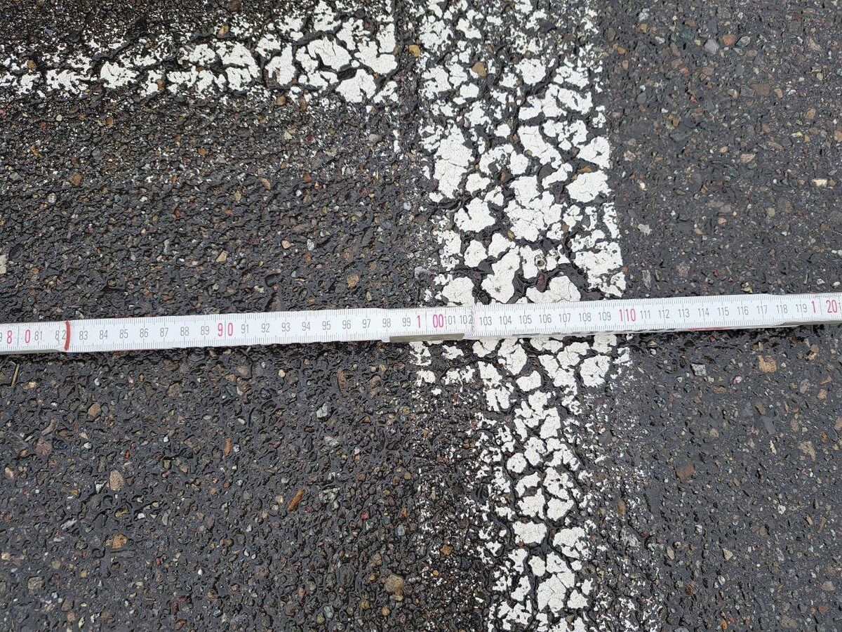 A road surface with a white line and a measuring tape across it.