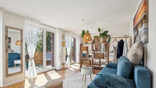 Un salon spacieux avec un grand canapé, une table basse et une bibliothèque. Une porte-fenêtre coulissante donne accès à un balcon.