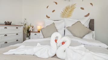 Habitación de hotel con una cama bien hecha, un aparador con cajones, una mesita de noche con lámpara y decoraciones en la pared con diseño de plumas y hojas de palma.