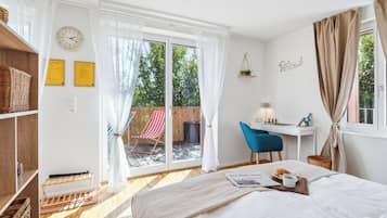 Ein Schlafzimmer mit Bett, Schreibtisch, Stuhl, einem Fenster mit Vorhängen, einer Uhr und Blick ins Freie.