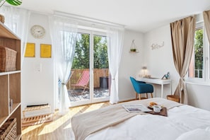 A bedroom with a bed, a desk, a chair, a window with curtains, a clock, and a view of the outdoors.