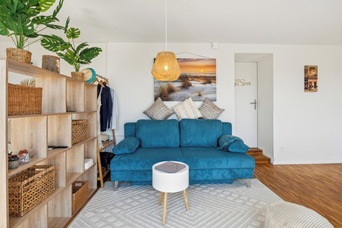 Ein modernes Wohnzimmer mit einem blauen Sofa, einem weißen Beistelltisch und einem großen Gemälde, das einen Sonnenuntergang zeigt.