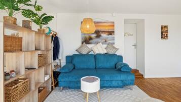 A modern living room with a blue sofa, a white side table, and a large painting of a sunset.
