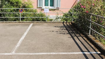 Un área de estacionamiento con valla metálica, señal de no estacionar y un edificio con ventanal.