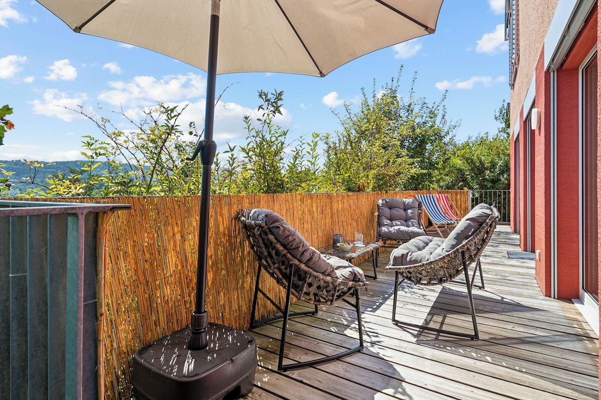 Eine Terrasse im Freien mit Holzboden, zwei Korbstühlen, einem Tisch und einem Sonnenschirm.