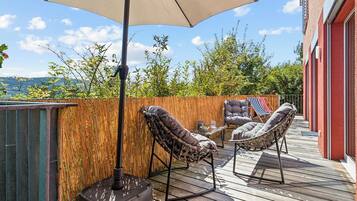 An outdoor deck with a wooden floor, two wicker chairs, a table, and an umbrella.