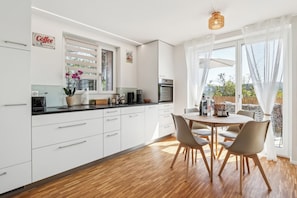 A modern kitchen with white cabinets, a dining area with a round table and chairs, and a view through large windows. - ReMo I Aare view I Business - Family - Terrace (Brugg)
