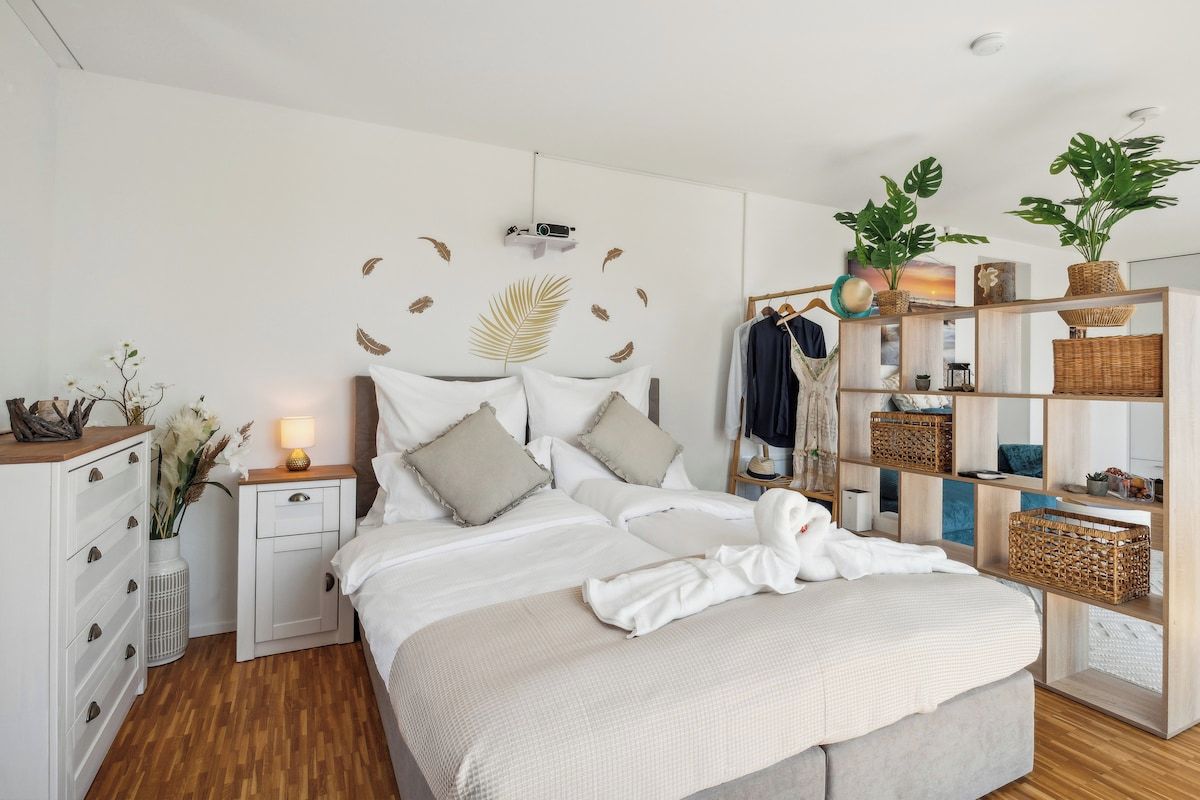 A modern bedroom with a bed, bedside tables, a wardrobe, and a shelving unit with plants.
