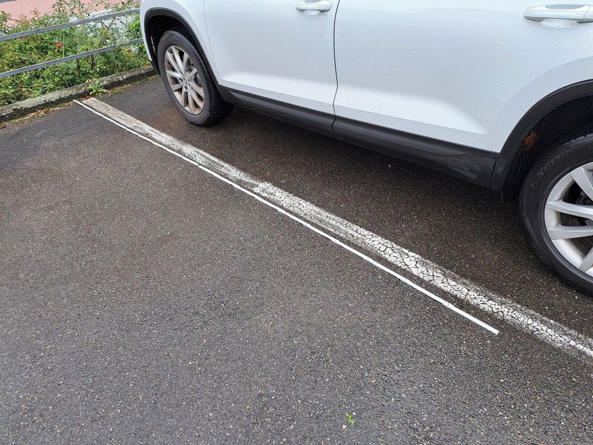 Un coche blanco aparcado en un espacio de estacionamiento delimitado por una línea blanca.
