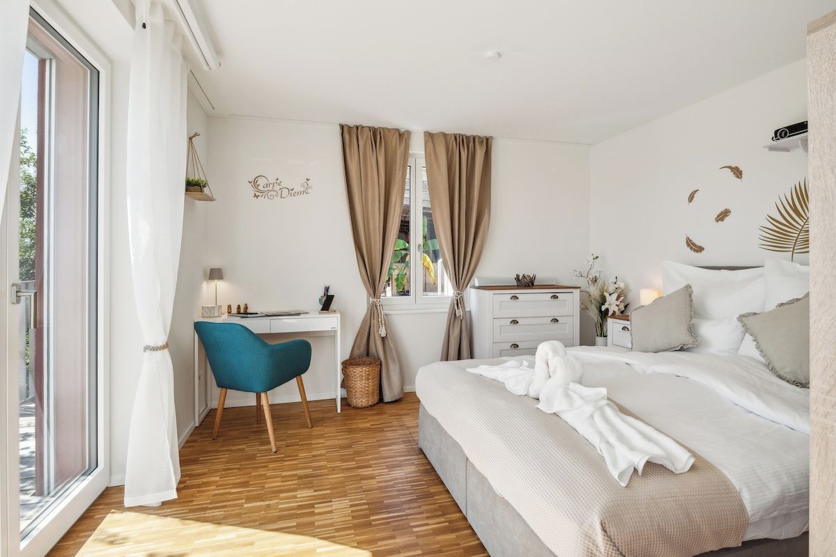 Ein Schlafzimmer mit einem Bett, einem Schreibtisch, einem Stuhl und einem Fenster mit Vorhängen.