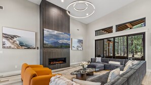 A modern living room with a fireplace, large windows, and a cozy seating area. - Large 5BR forest lodge w fireplace, wine cooler! (Flagstaff)