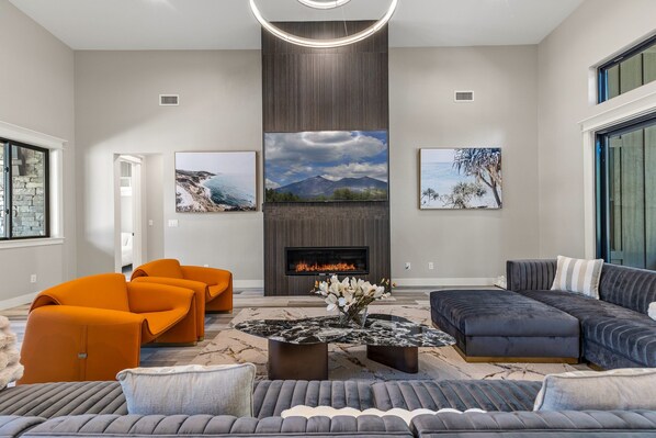 Een moderne woonkamer met een open haard, oranje en grijze banken en kunstwerken aan de muur.