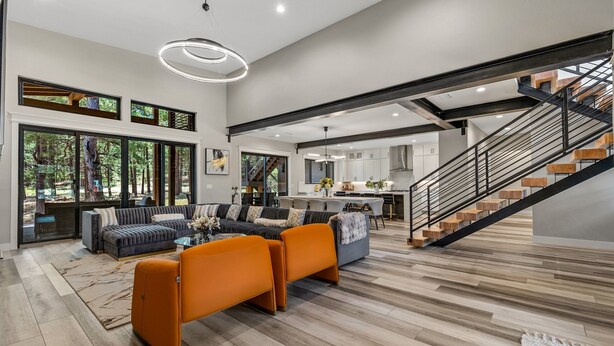 A spacious living area with a large sofa, a coffee table, and a staircase leading to an upper level. - Large 5BR forest lodge w fireplace, wine cooler! (Flagstaff)