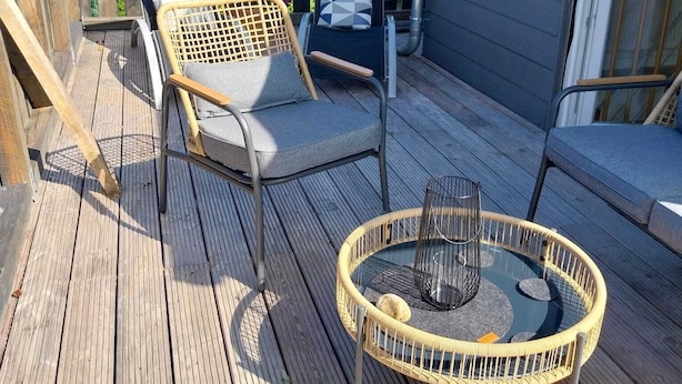 A wooden deck with two wicker chairs, a glass table, and a railing.