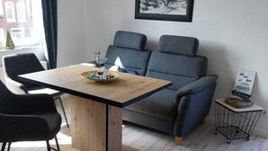 A modern living room with a wooden dining table, grey sofa, and a framed picture on the wall.