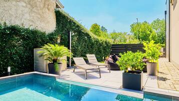 Piscina con sillas de descanso y plantas en macetas.